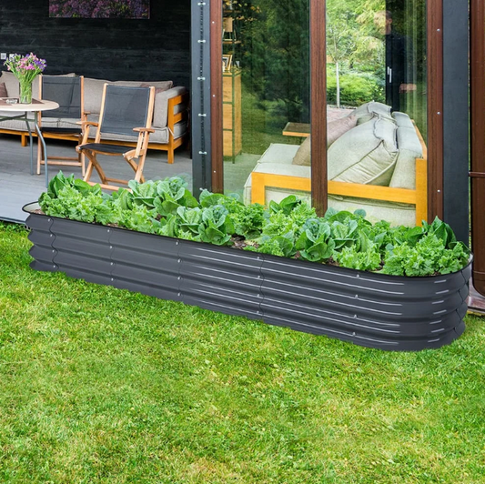 Black metal raised garden bed with green plants on a grassy area, with a patio and outdoor furniture in the background.